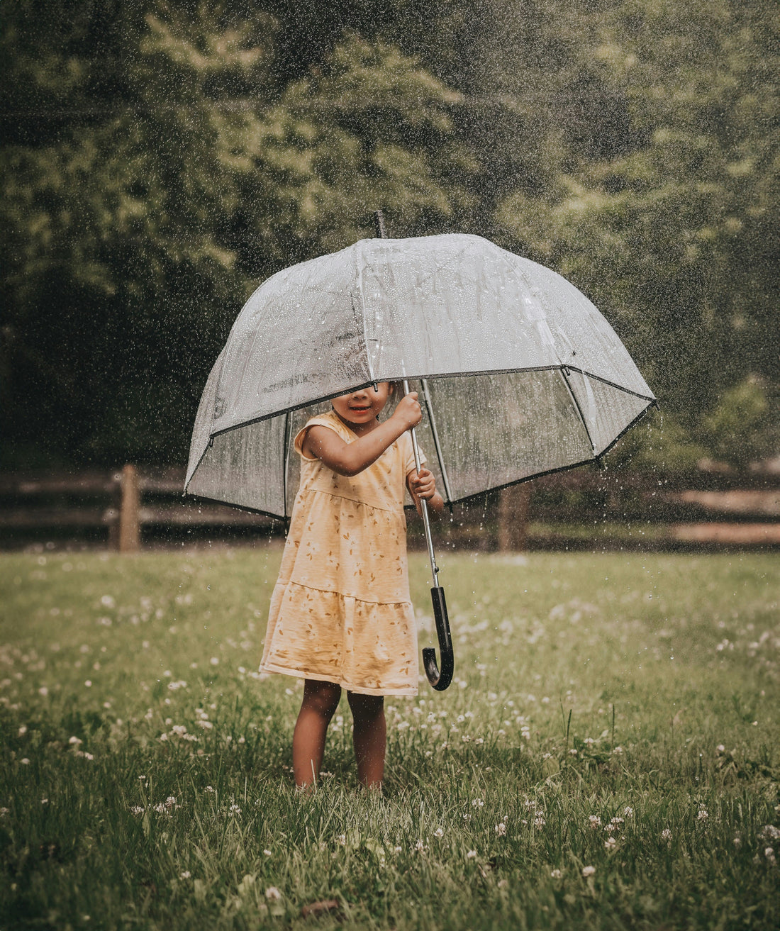 A young child playing outside in the rain with a large umbrella