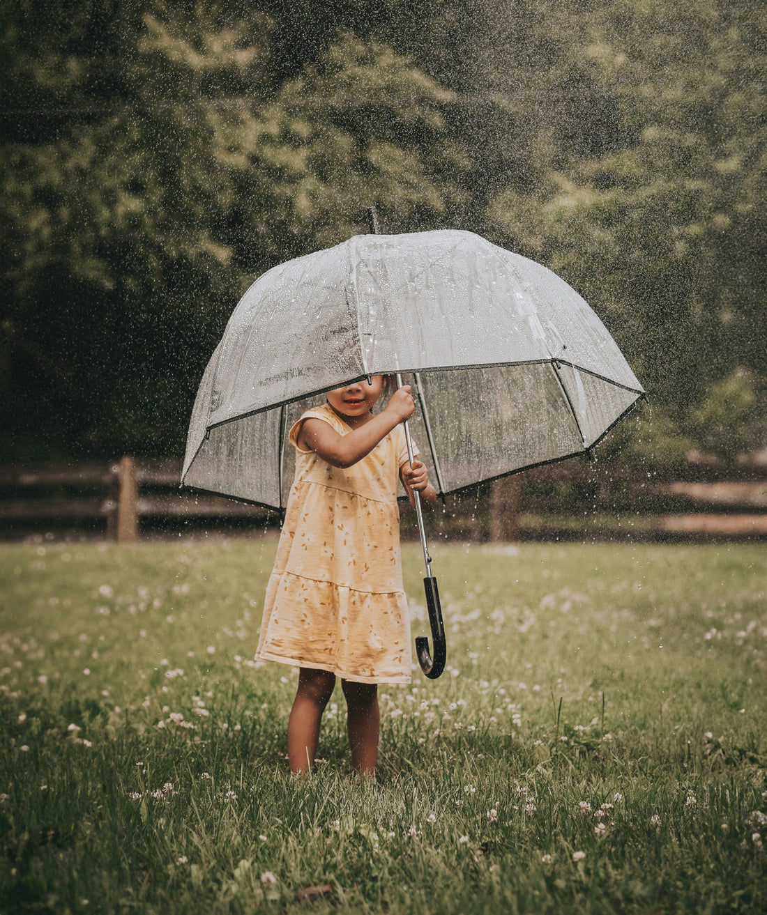 A young child playing outside in the rain with a large umbrella
