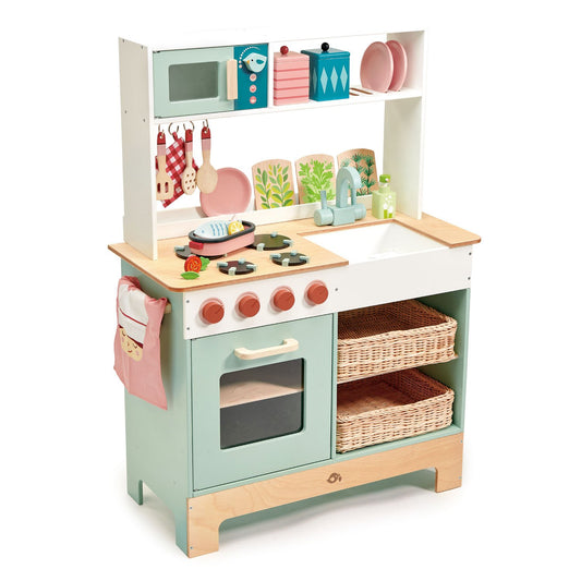 A wooden play kitchen for children with a green oven, beige counters, and pink accents, including decorative plates, utensils, and a pizza oven detail.