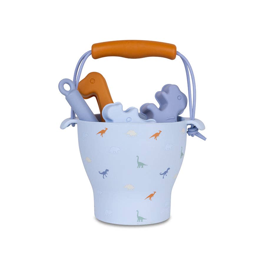 A blue plastic bucket with a dinosaur beach play set, including a shovel and various dino-shaped molds.