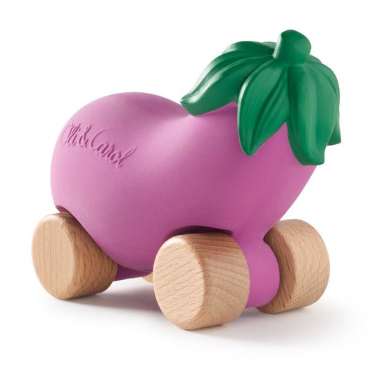 Pink toy eggplant with wooden wheels and a green leaf on a white background