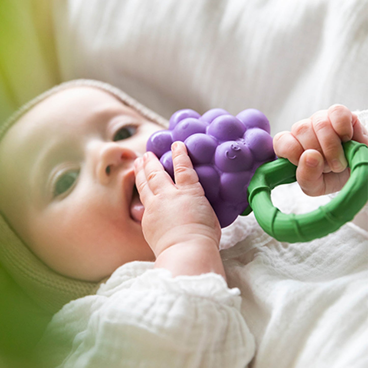 Baby holding a purple teething toy with green handle