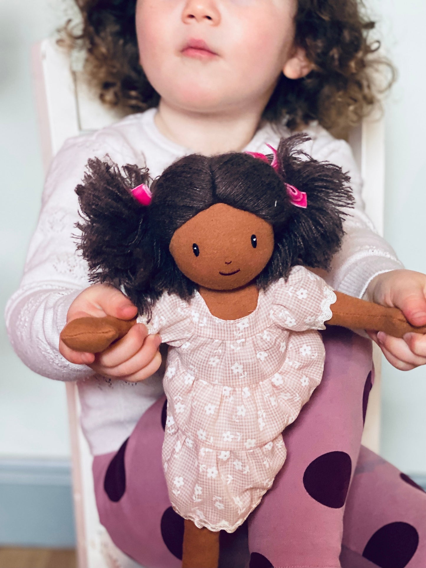 Child holding a doll with dark hair and pink bows, sitting on a purple cushion.