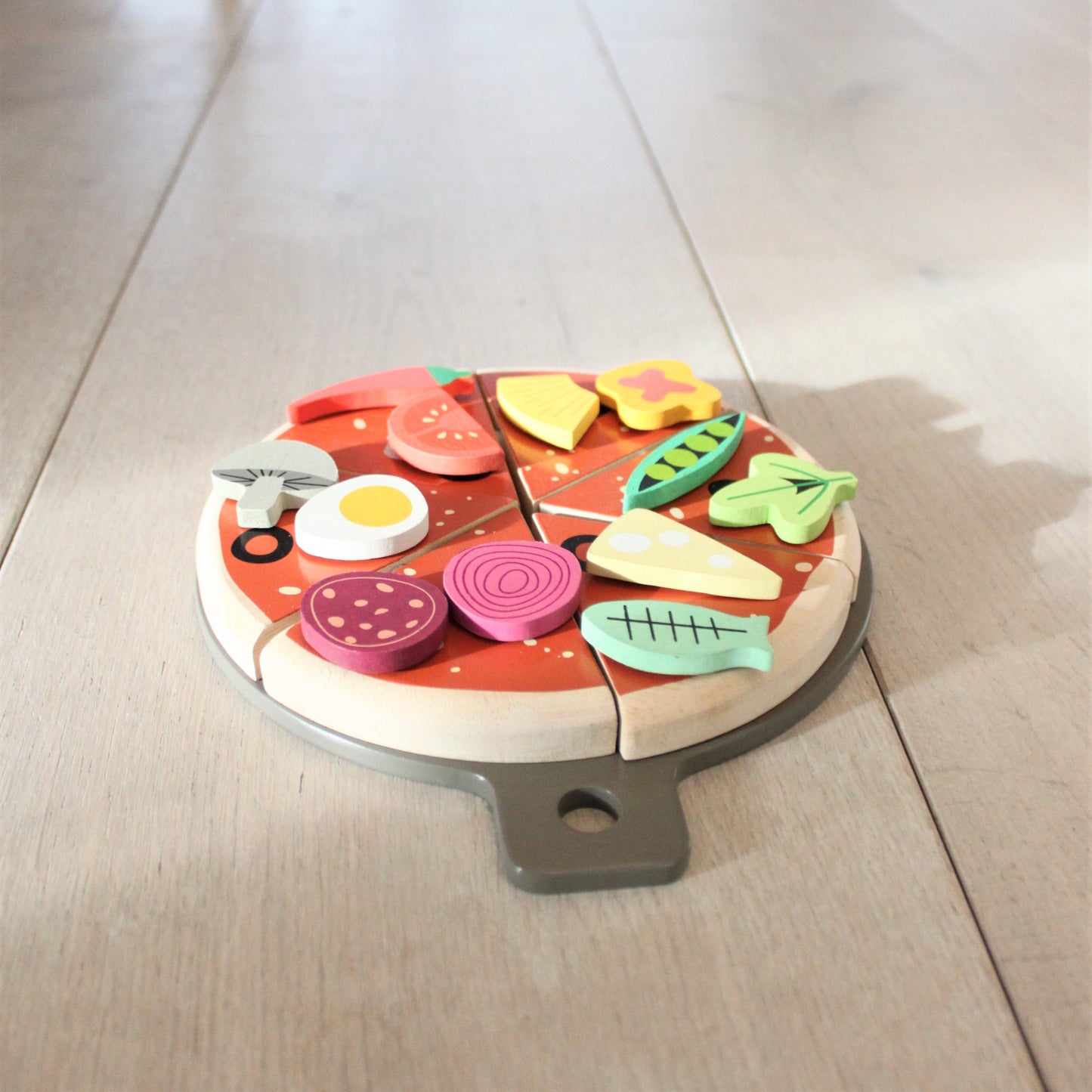 Wooden pizza toy with colorful slices on a light wooden floor