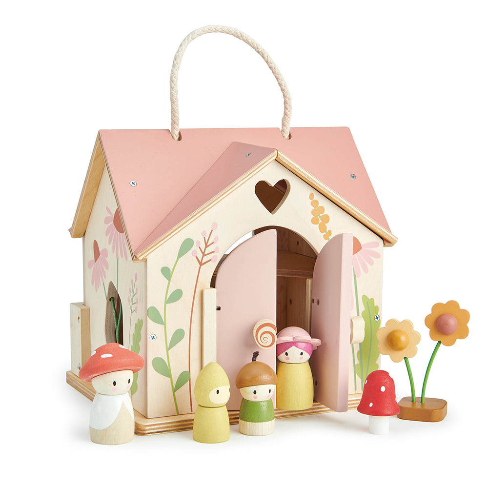 A rose-colored wooden dollhouse with a thatched roof, featuring a family of toy figures including a man, woman, and child, along with a toadstool and flowers.
