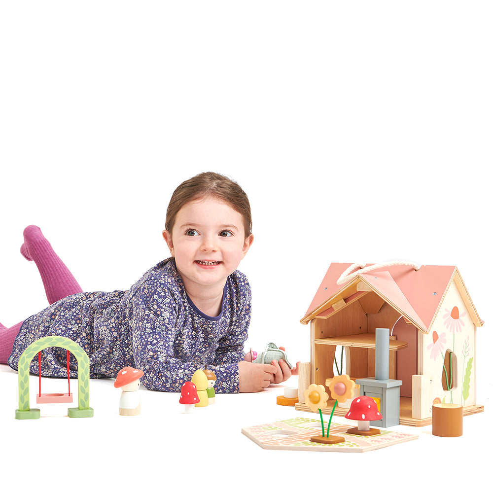 Child playing with a dollhouse and accessories on a white background. Tender Leaf Toys Rosewood cottage.