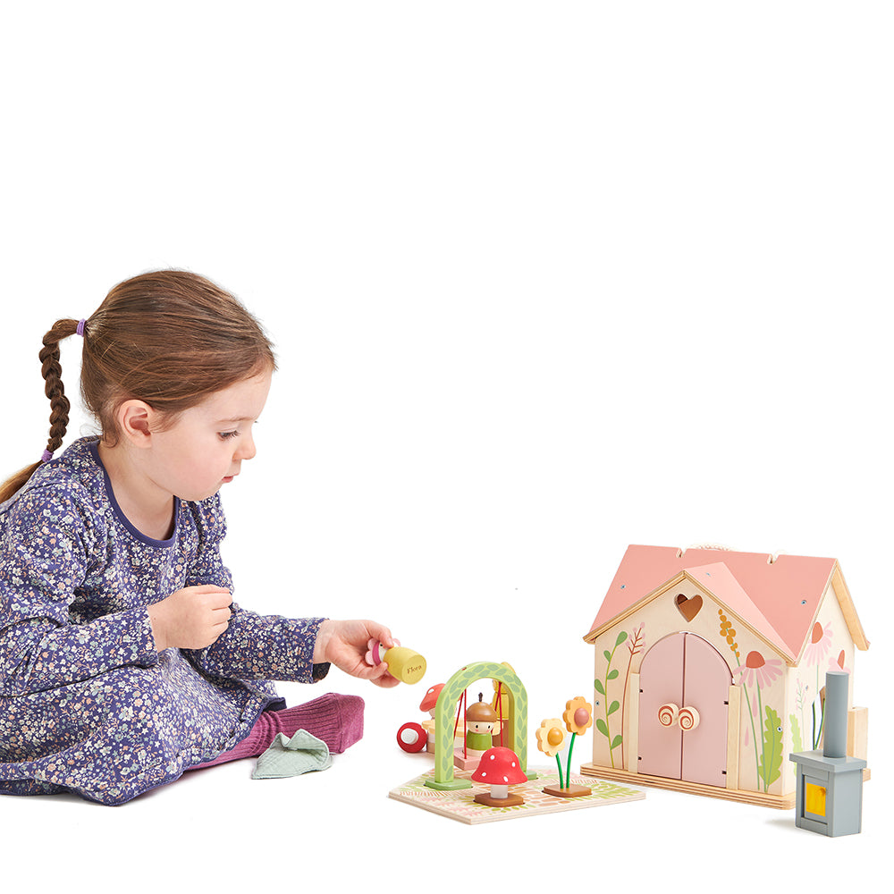 Child playing with a wooden dollhouse and accessories on a white background. Tender Leaf Toys Rosewood cottage.