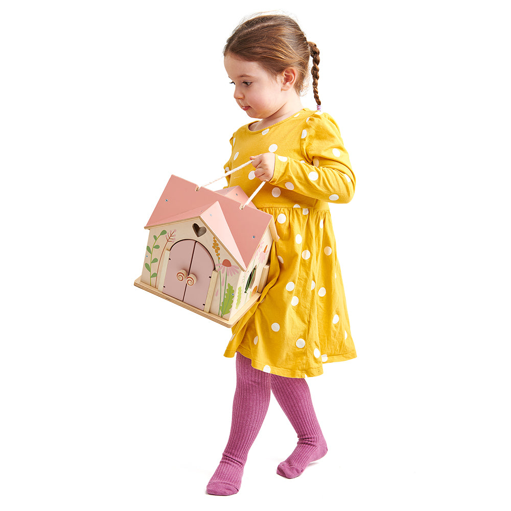 Child in a yellow dress holding a pink fairy house on a white background. Tender Leaf Toys Rosewood cottage.