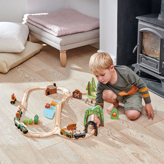 Child playing with a wooden train set on a wooden floor in a cozy living room. Tender Leaf Toys Wild Pines Train Set