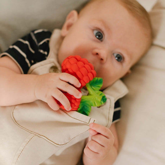 Baby holding a red and green toy, lying on a beige surface