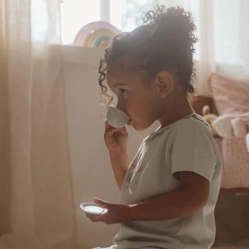 Child playing with a tea set in a softly lit room. Little Dutch Fairy Garden Tea Set