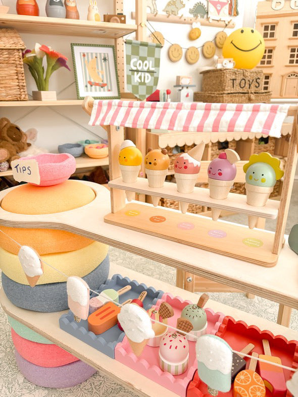 Toy ice cream stand with various toy ice cream cones and a toy cash register on a shelf.