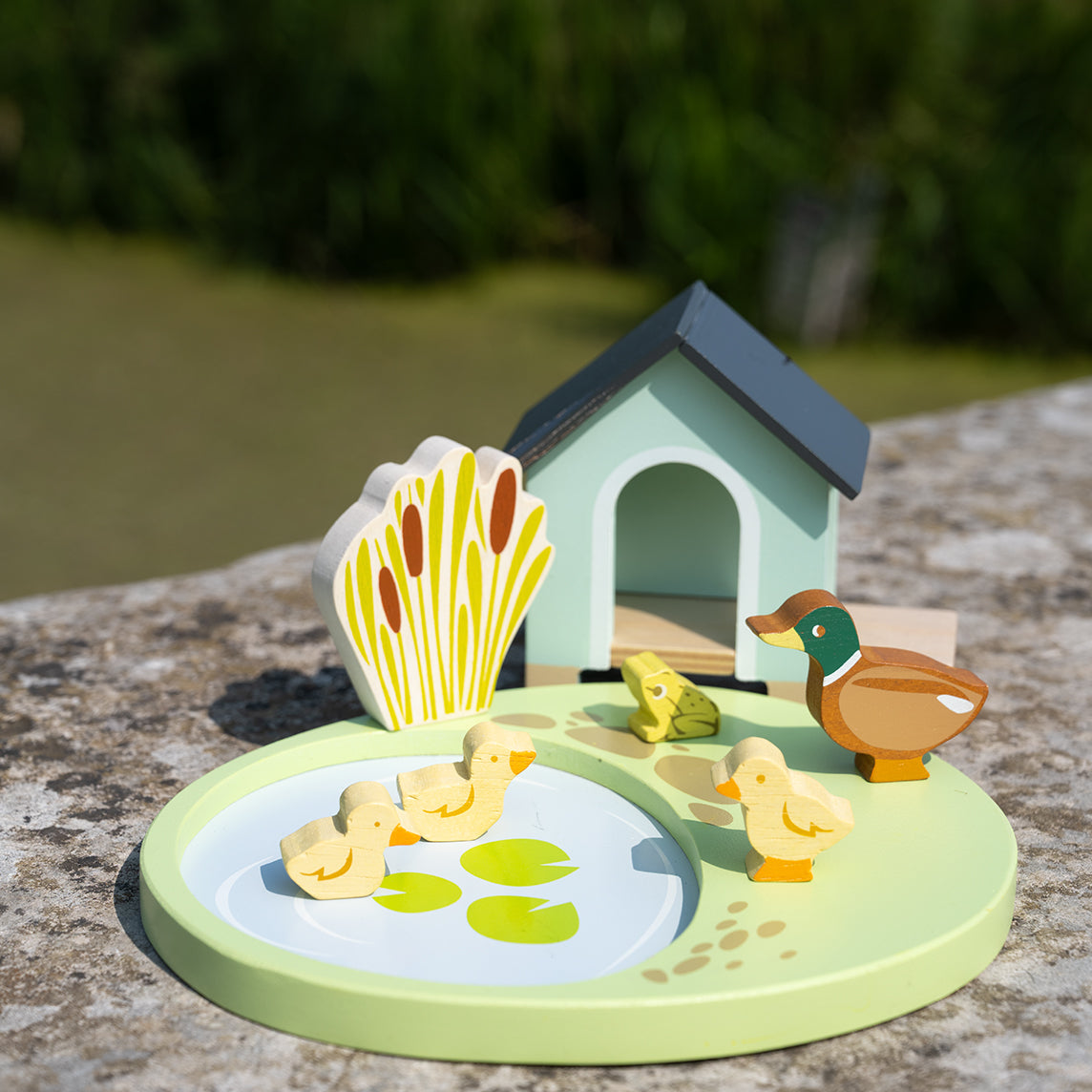 Toy set with ducks, ducklings, and a duck house on a stone surface with a natural background.