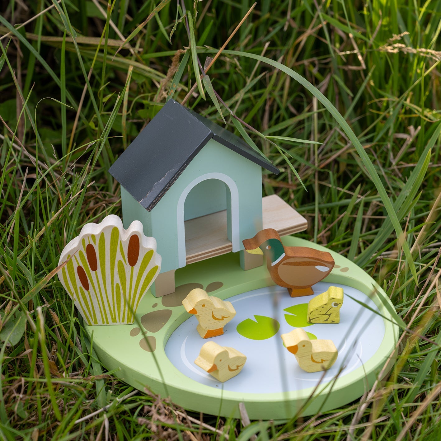 Wooden duck pond toy with ducks and a duck house on grass