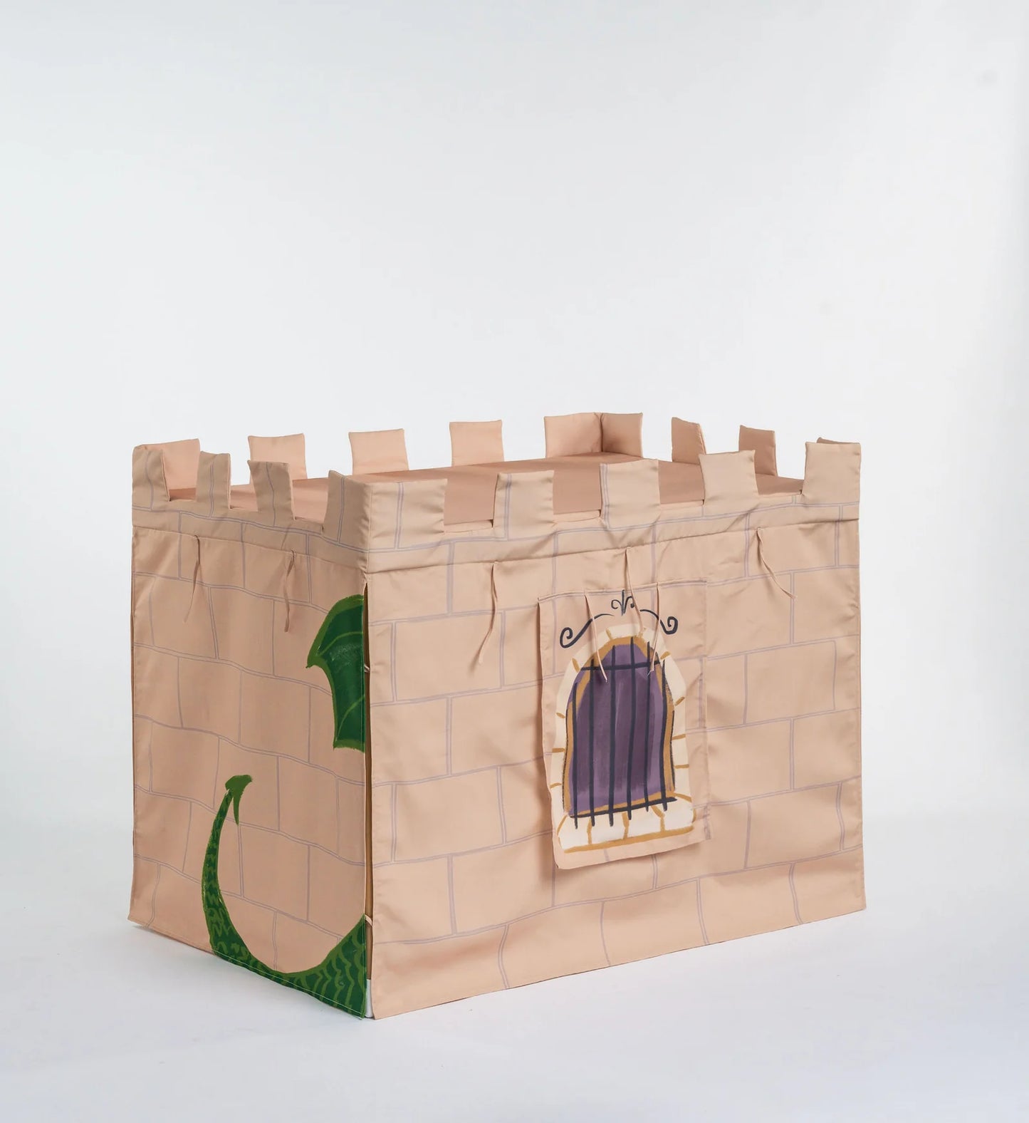 A castle-themed storage bin made from tan cardboard or paperboard, printed with a brick pattern, crenellated top, a window with purple shutters, and a green dragon illustration on the side, photographed on a white studio background.