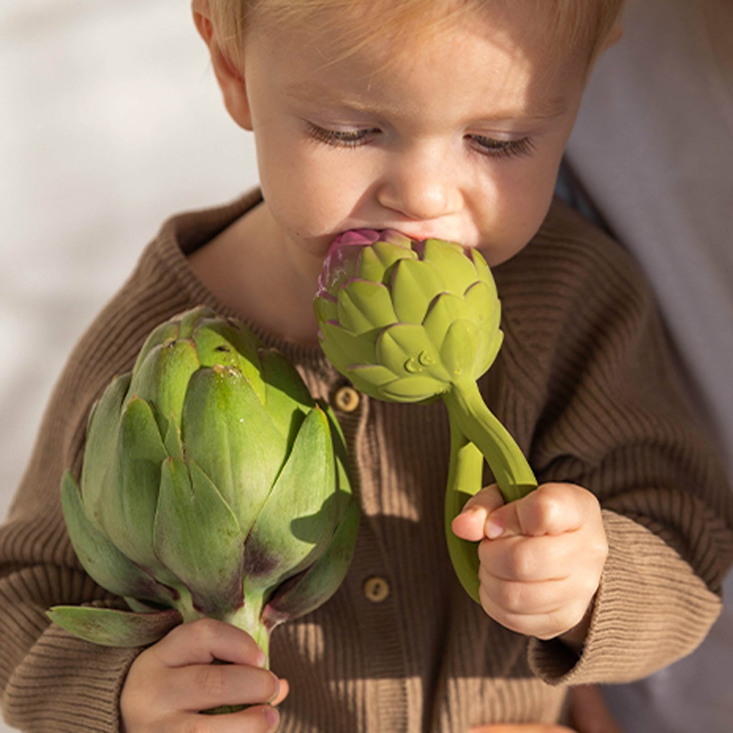 Child holding and playing with two artichokes against a neutral background