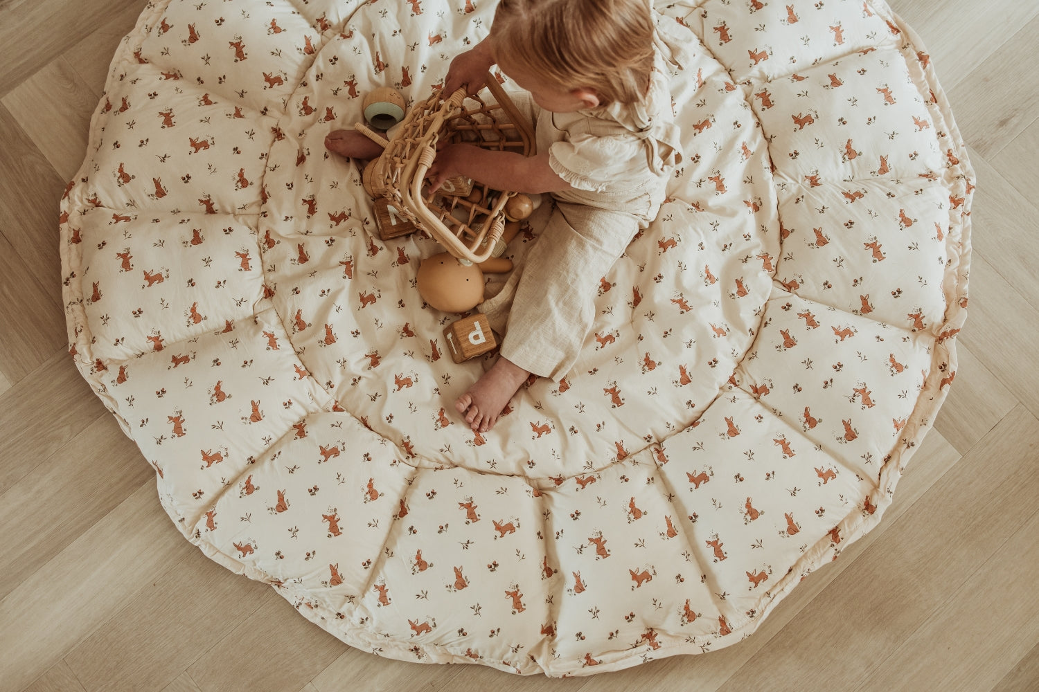 Child playing on a large round mat with animal patterns on a wooden floor.