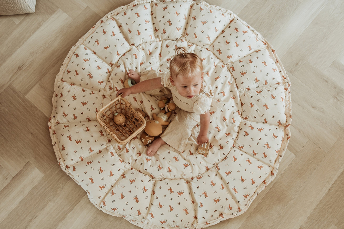 Child playing on a large round mat with a floral pattern on a wooden floor.