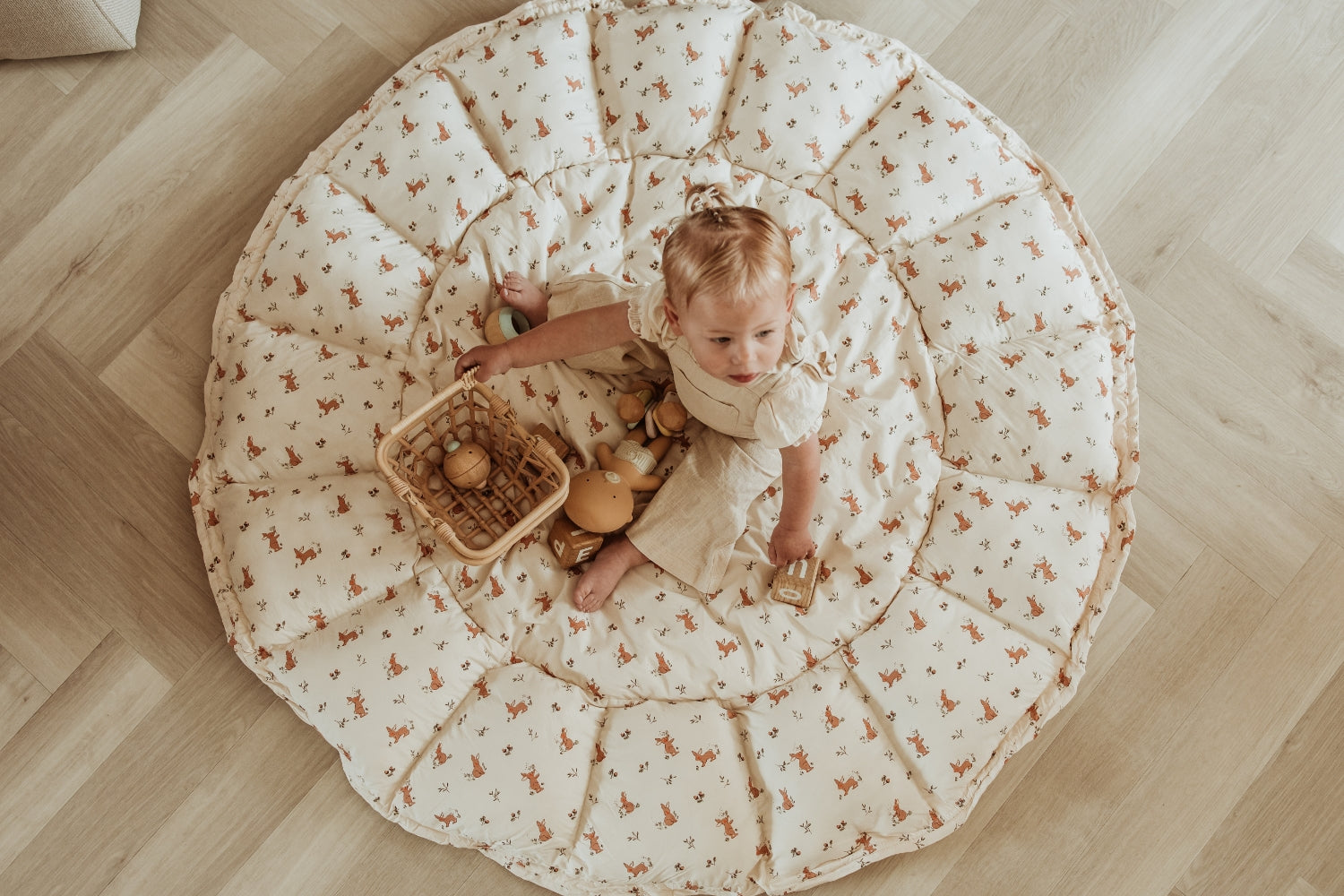 Child playing on a large round mat with a floral pattern on a wooden floor.
