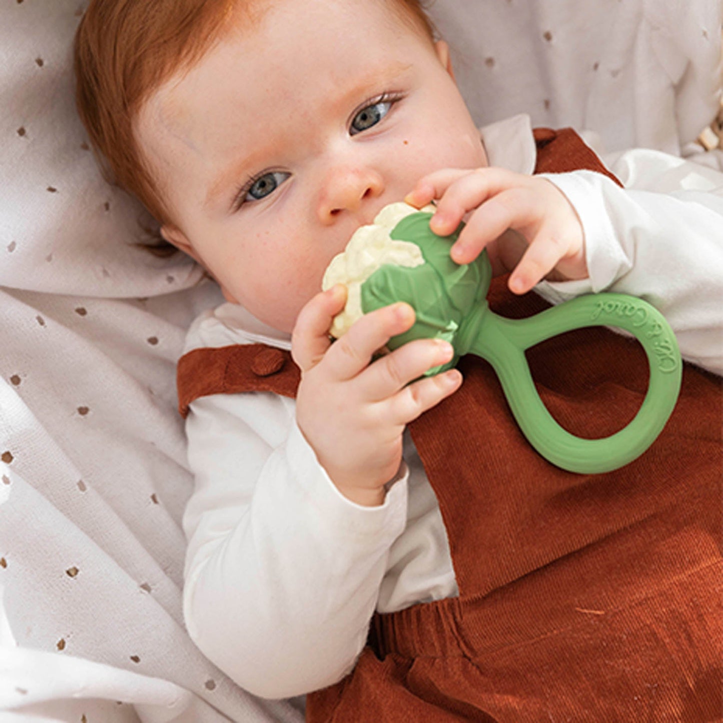 Baby holding a green teething toy with a soft background