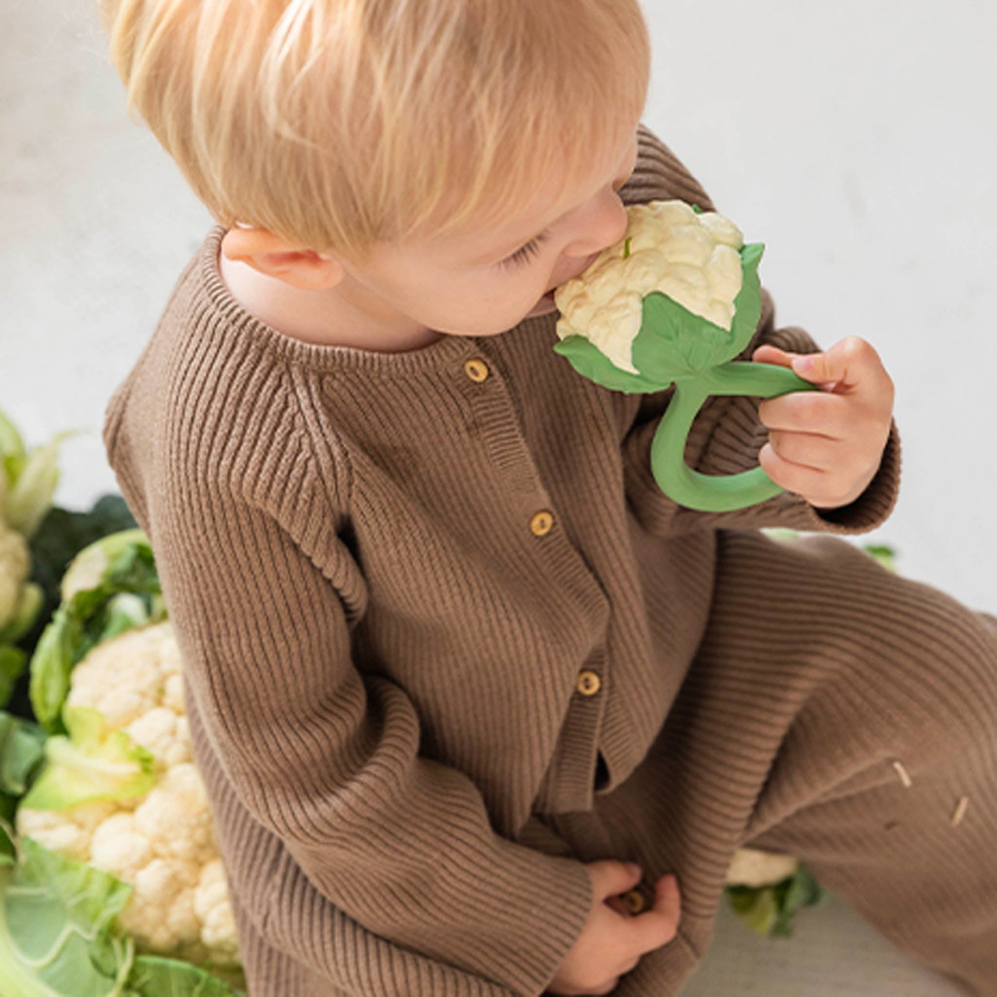 Child holding a toy cauliflower among real cauliflowers