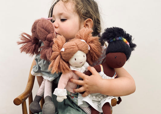Child holding three dolls with different hairstyles and outfits against a plain background