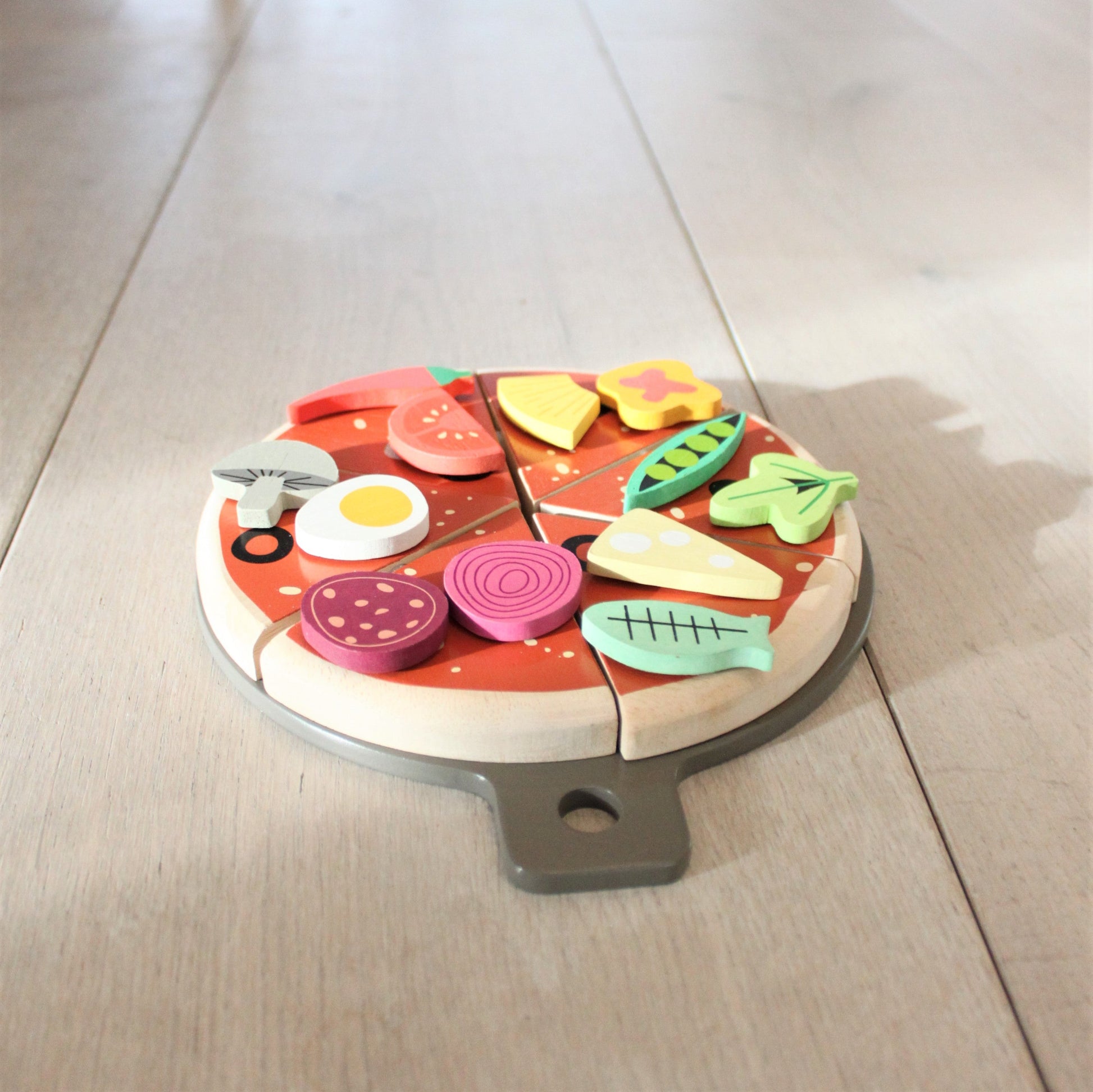 Wooden pizza toy with colorful slices on a light wooden floor