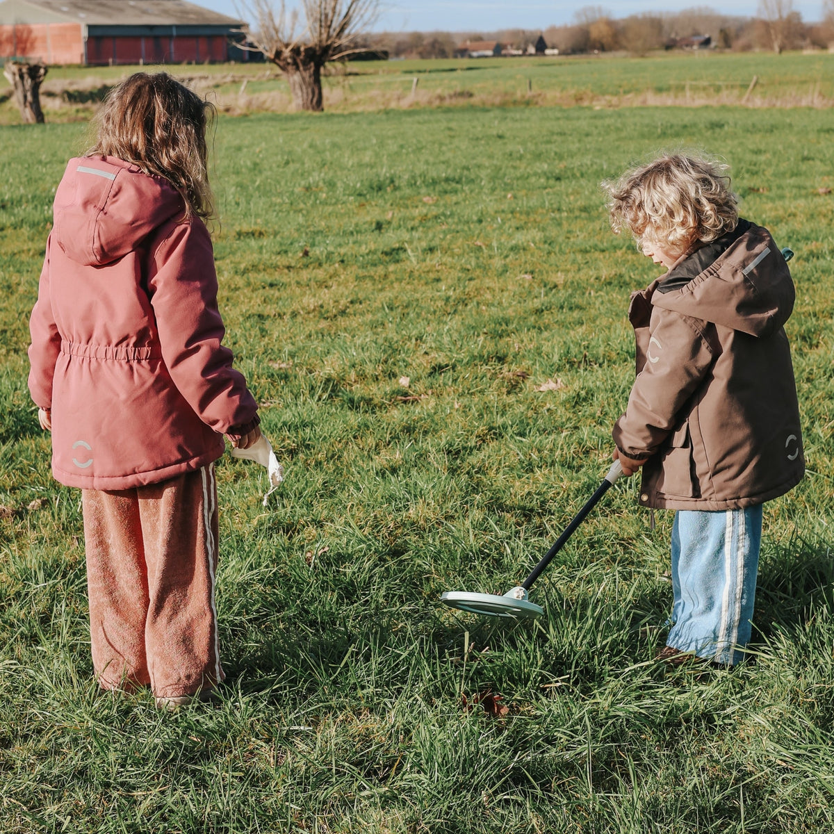 Two children in a field with one using a metal detector