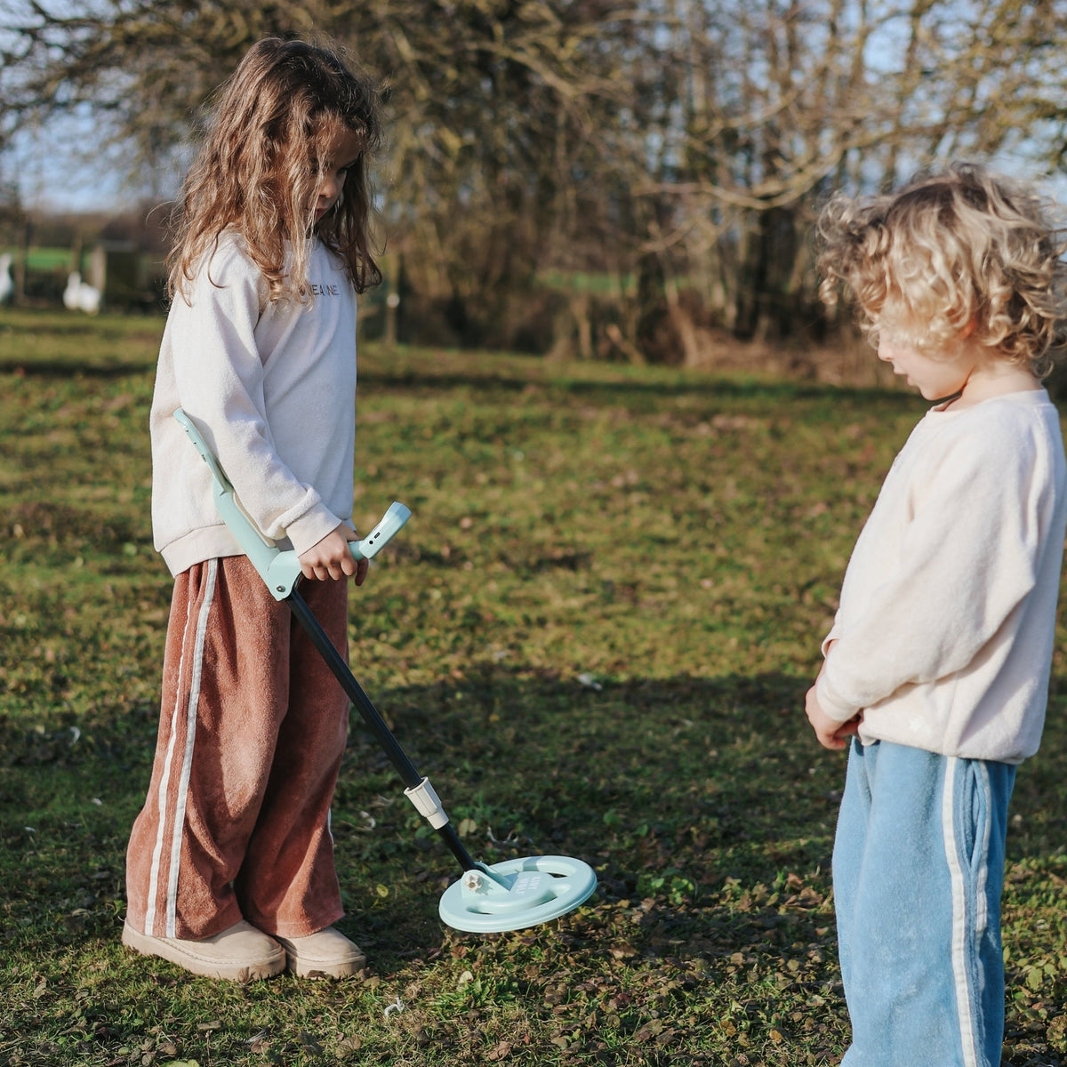 Two children playing with a toy metal detector in a grassy field.