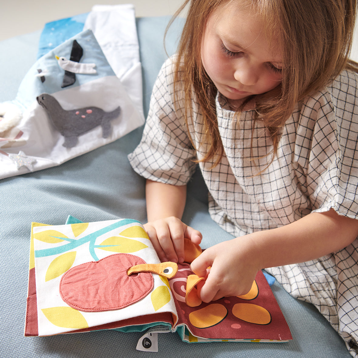 Child playing with a colorful soft book on a bed