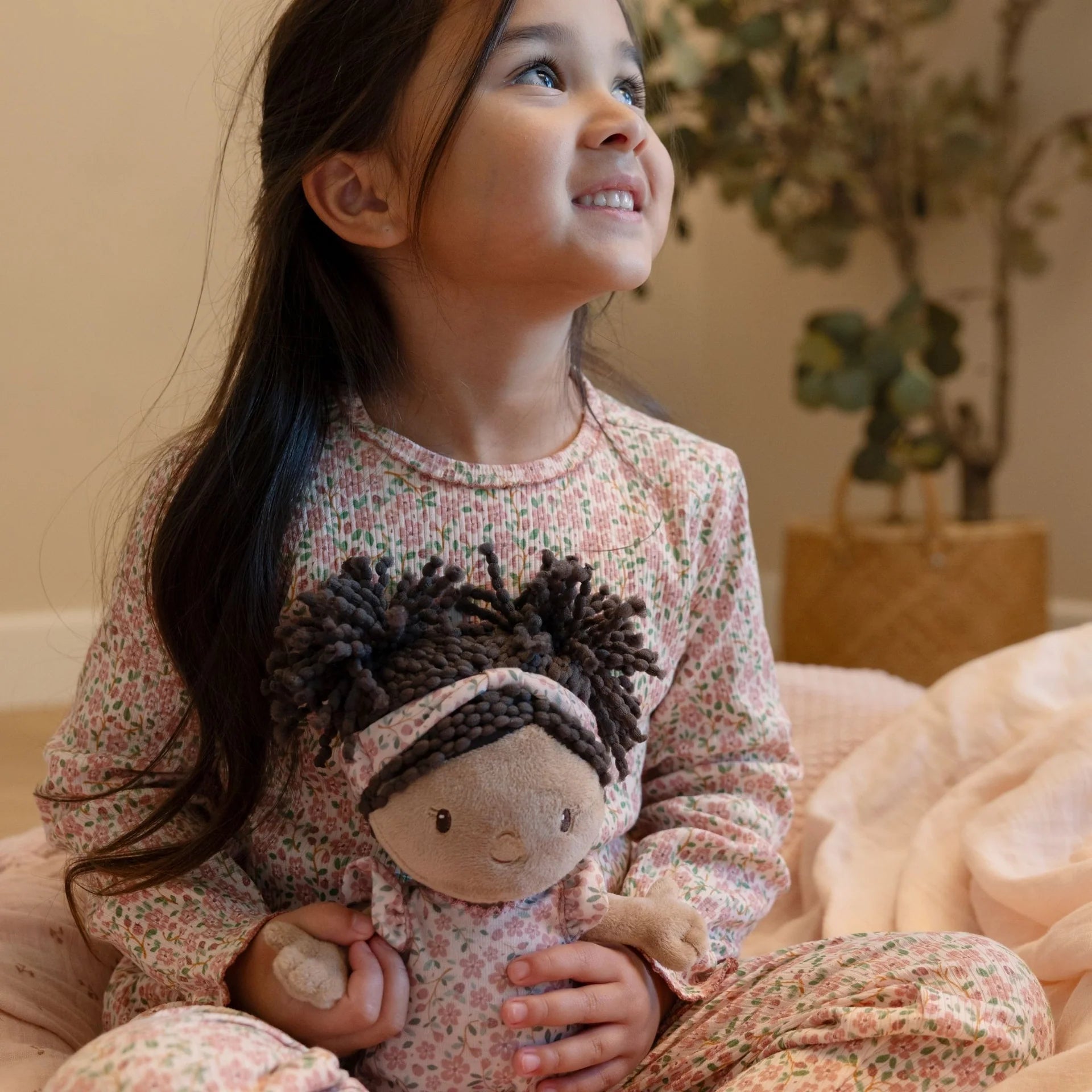 Young girl holding a plush toy with braided hair, sitting on a couch.
