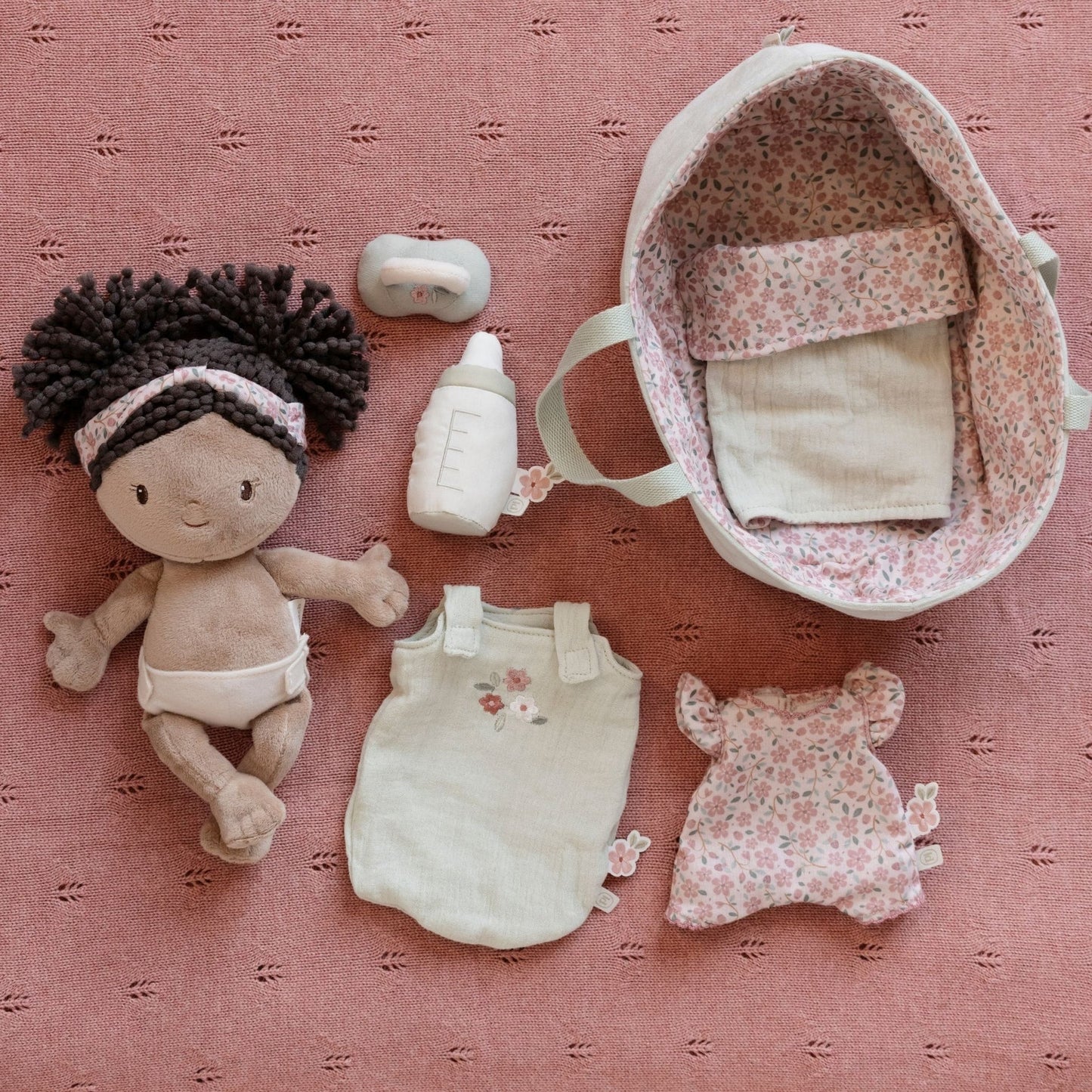 Baby doll and accessories on a pink textured surface