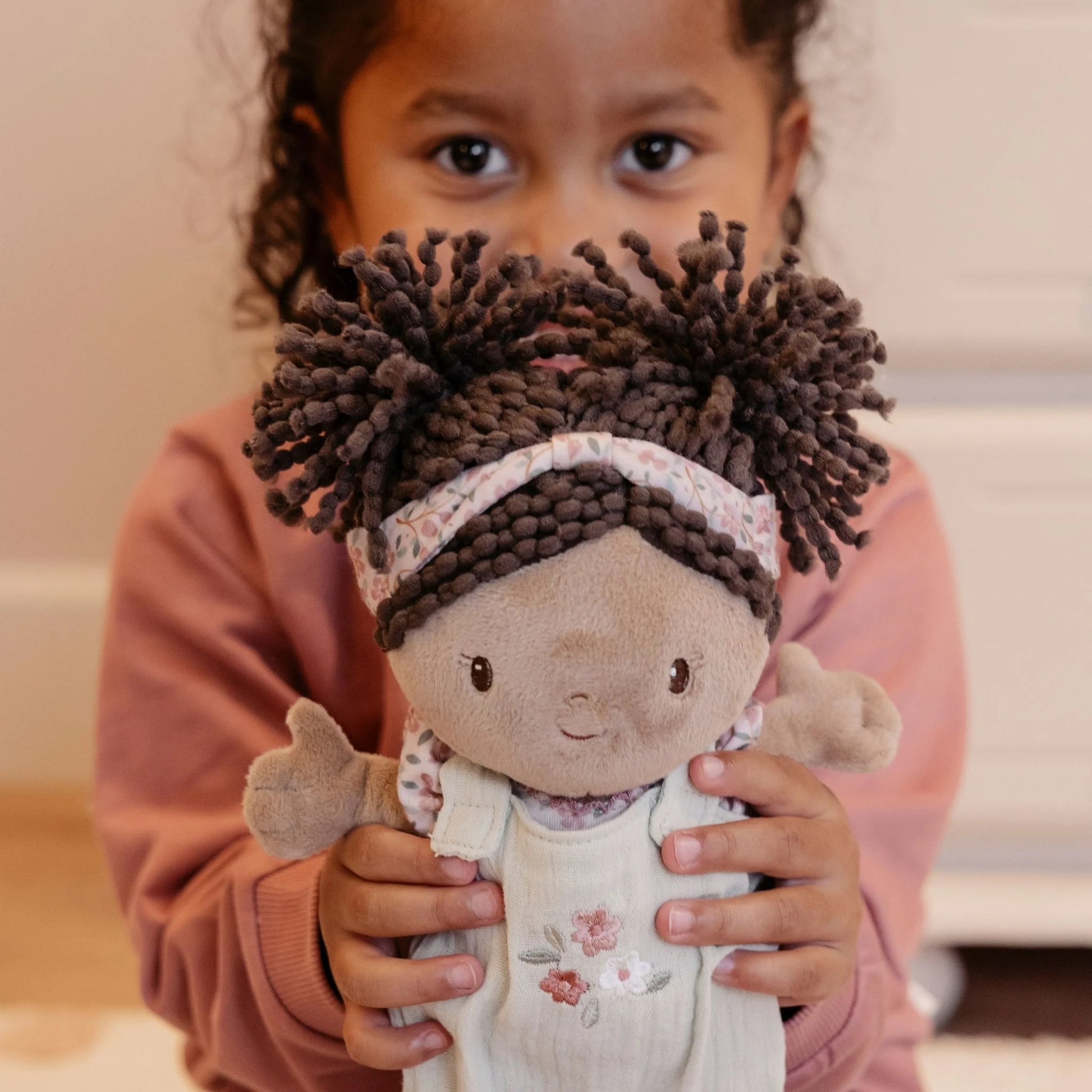 Child holding a plush toy with brown hair and a pink outfit.