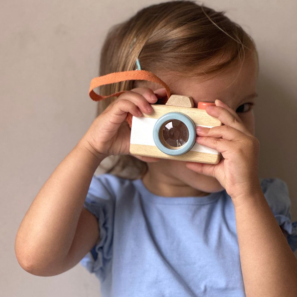Child holding a wooden toy camera against a plain background