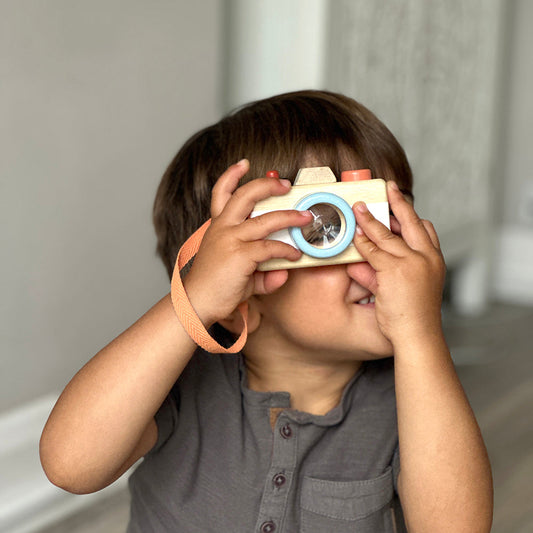 Child holding a toy camera up to their face with a neutral background