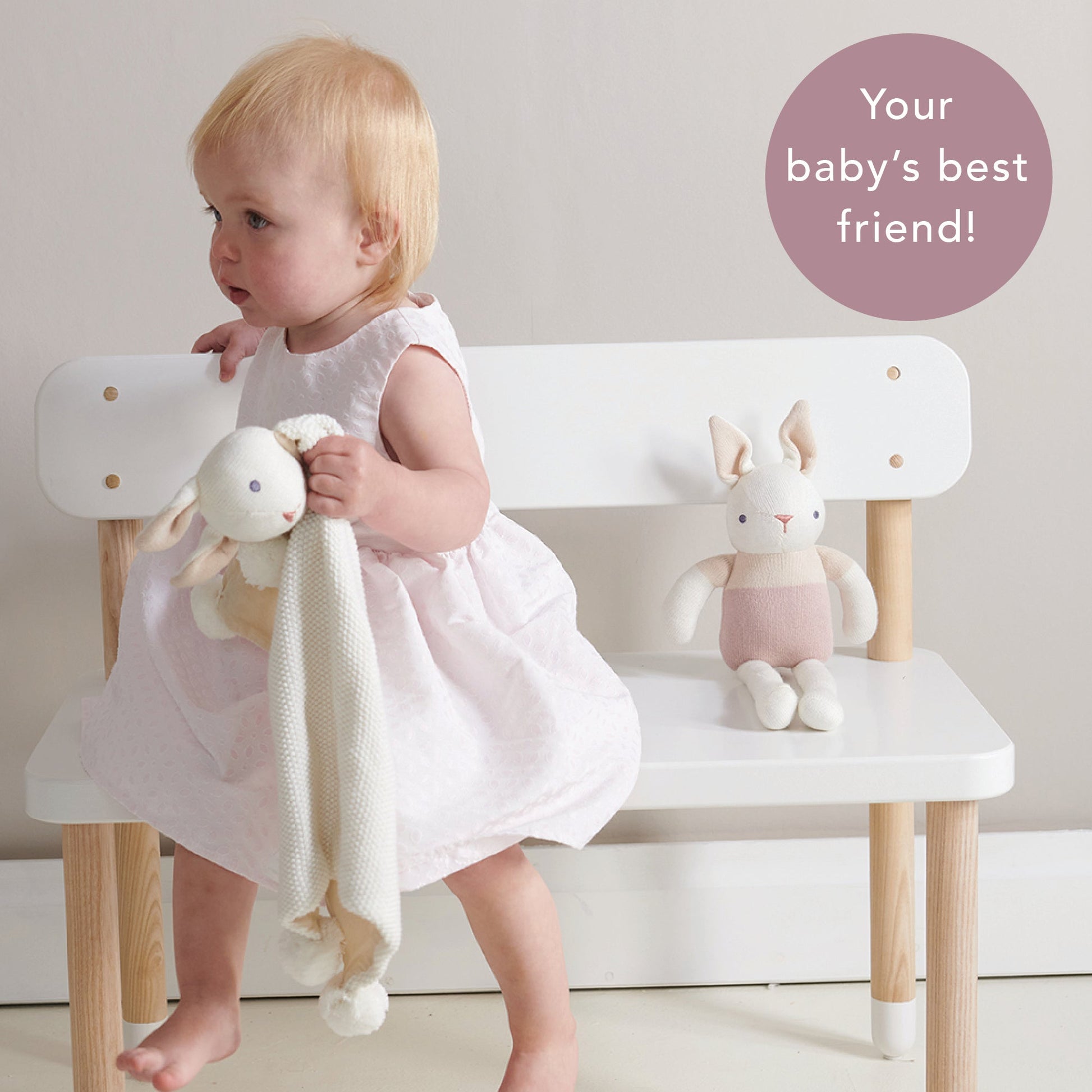 Child in a white dress sitting on a wooden chair with plush toys, text 'Your baby's best friend!' in the corner.