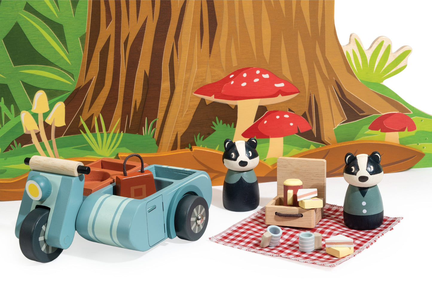 Toy scooter with sidecar and two animal figures in a forest setting with mushrooms and picnic setup.