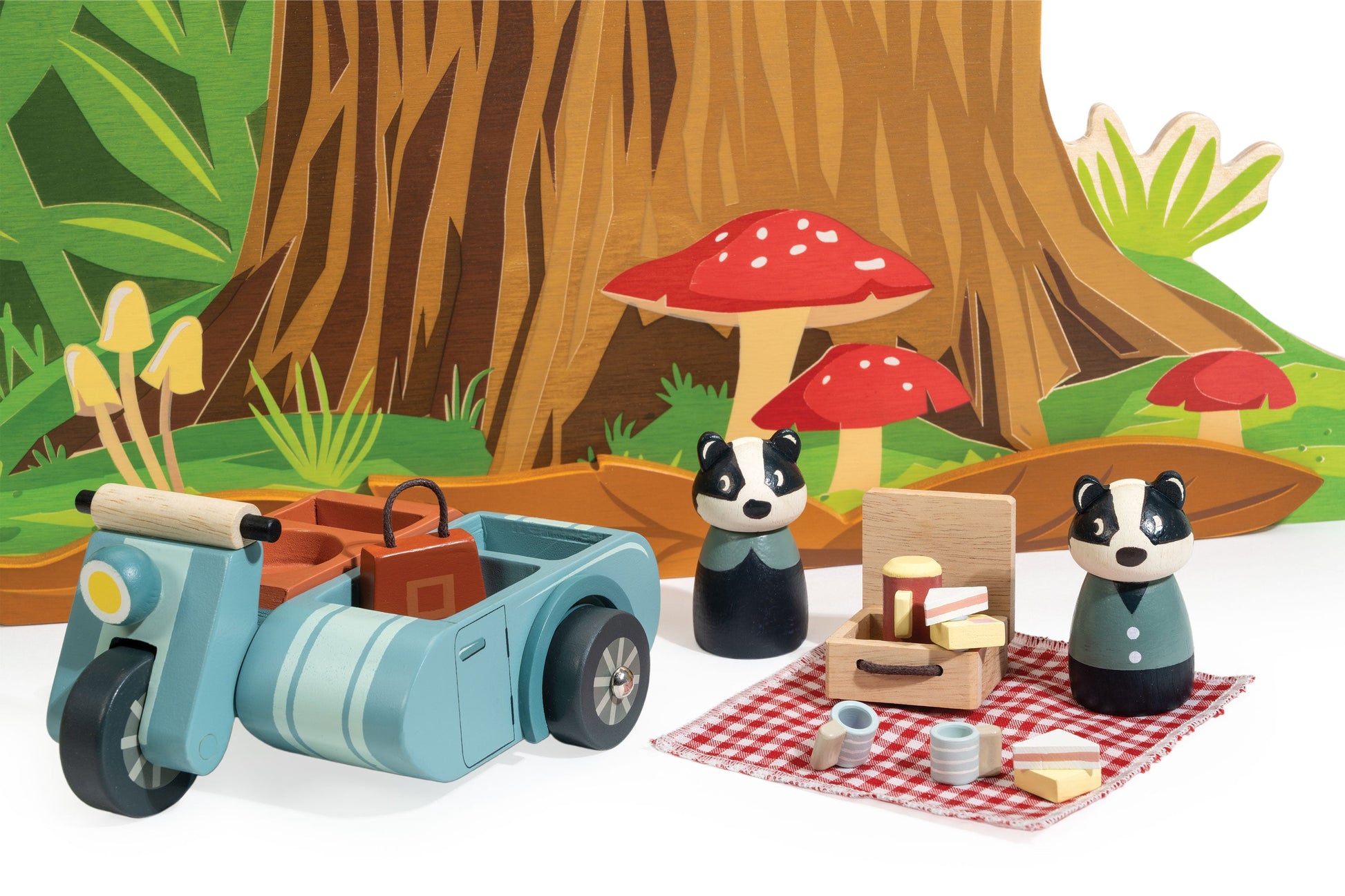 Toy scooter with sidecar and two animal figures in a forest setting with mushrooms and picnic setup.