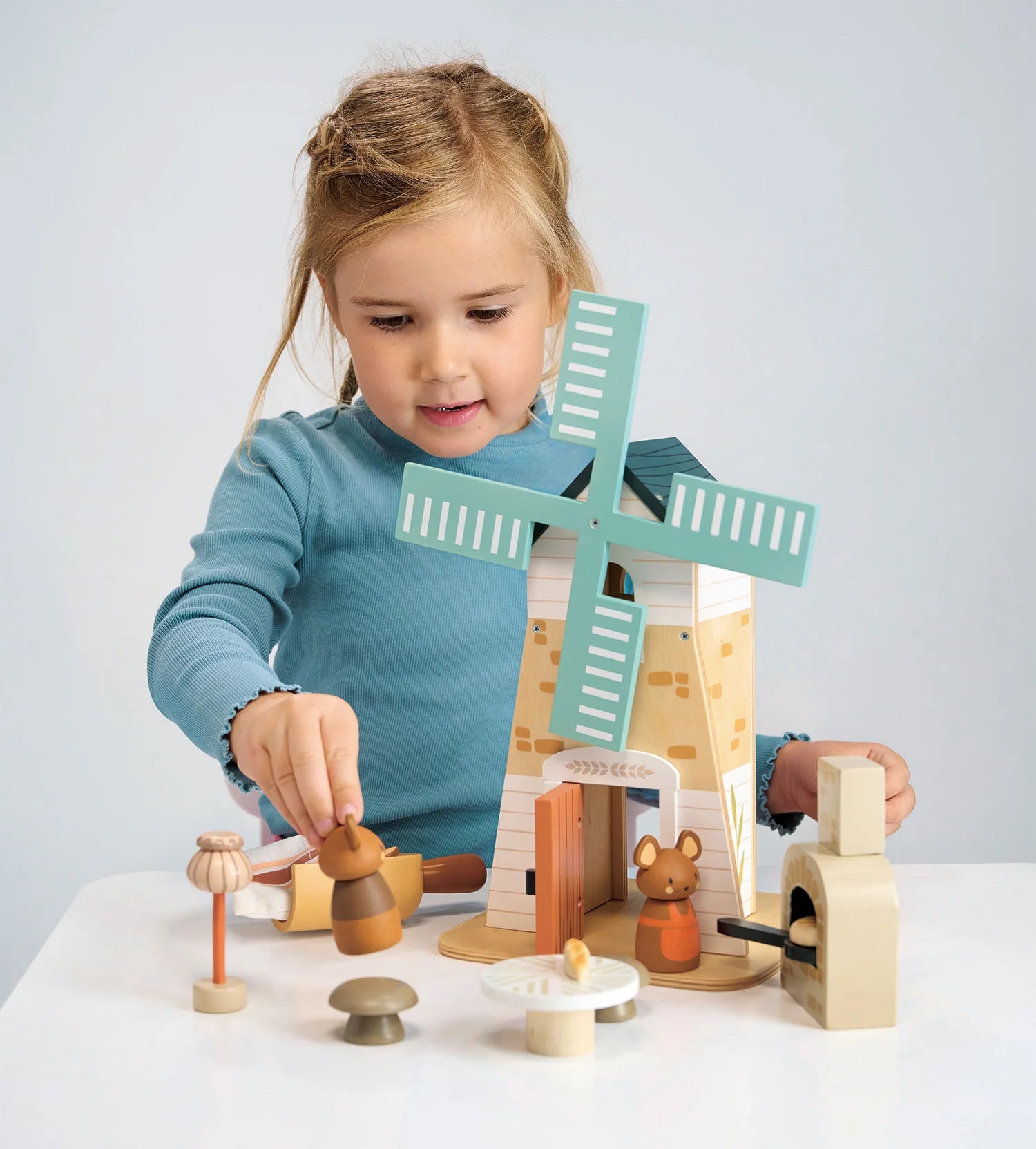 Child playing with a wooden toy windmill set on a white surface. Tender Leaf Toys Penny Windmill