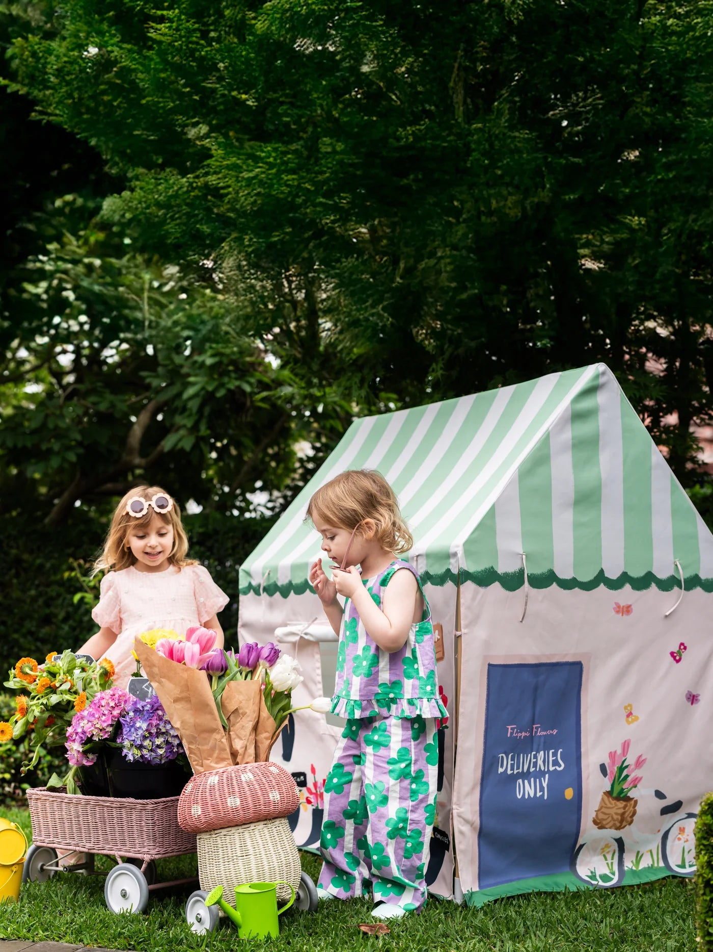 Two children playing with a green and white striped play tent in a garden.