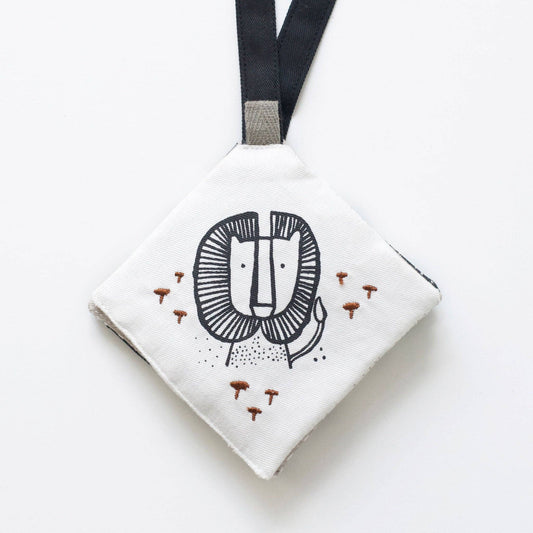 A crinkle pages stroller toy with an illustration of a lion's face in black and brown colors on a white background, attached to a black strap.