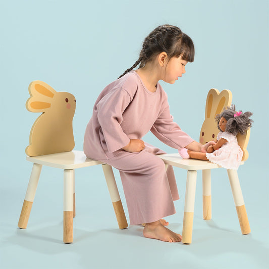 Child playing with a doll on a chair with rabbit ears against a light blue background