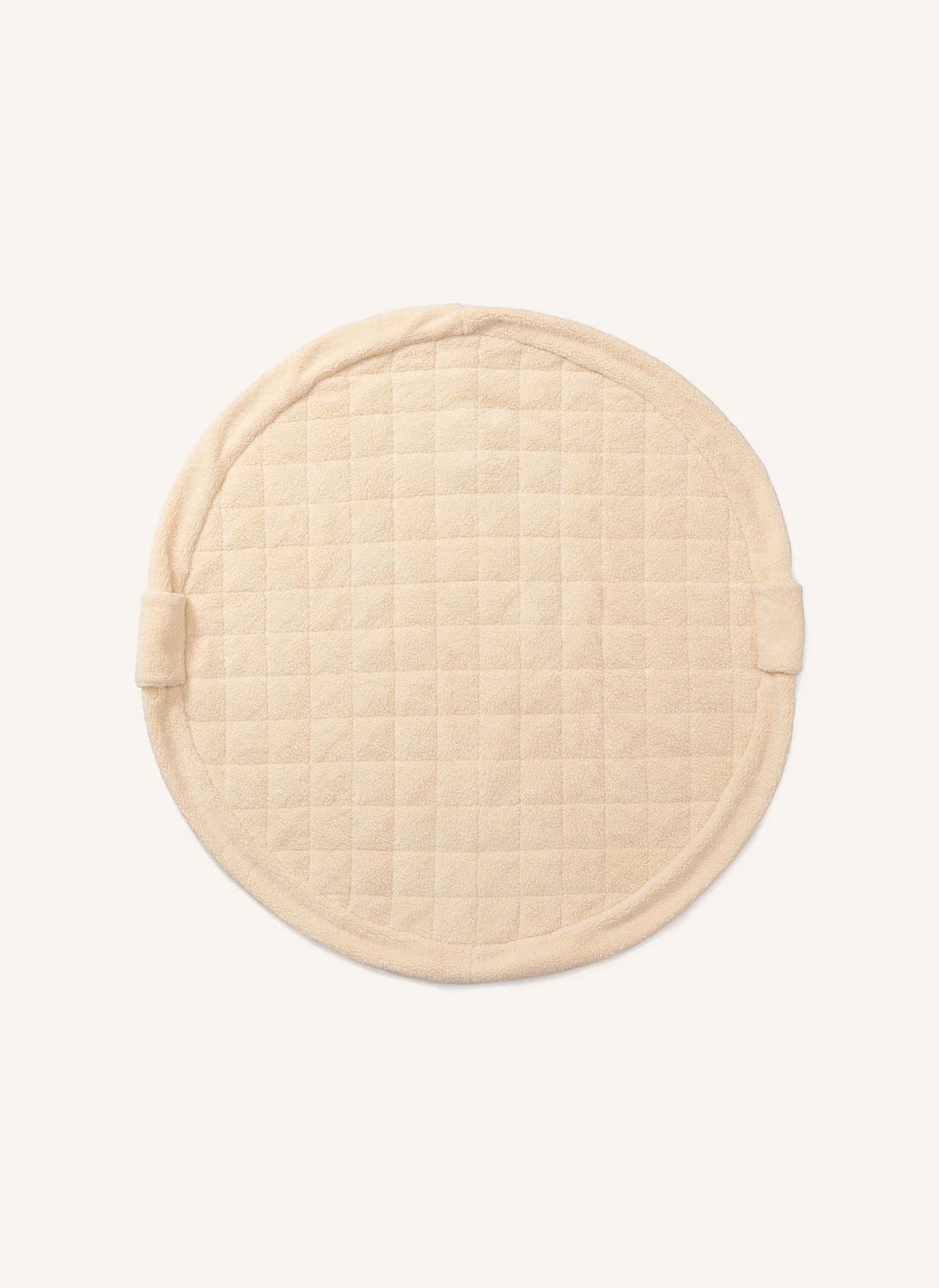 A round quilted fabric pad in a light cream or beige color, featuring a stitched grid pattern and small side tabs, shown against a plain off-white background.