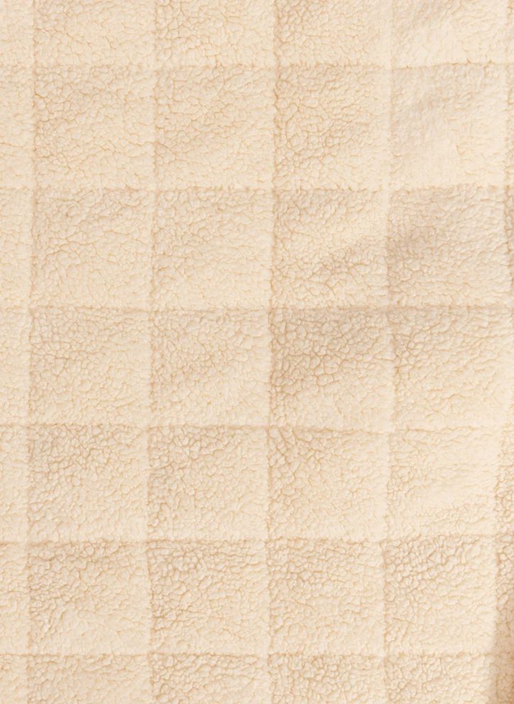 A close-up of a soft, textured cream-colored fabric with a subtle checkered pattern.