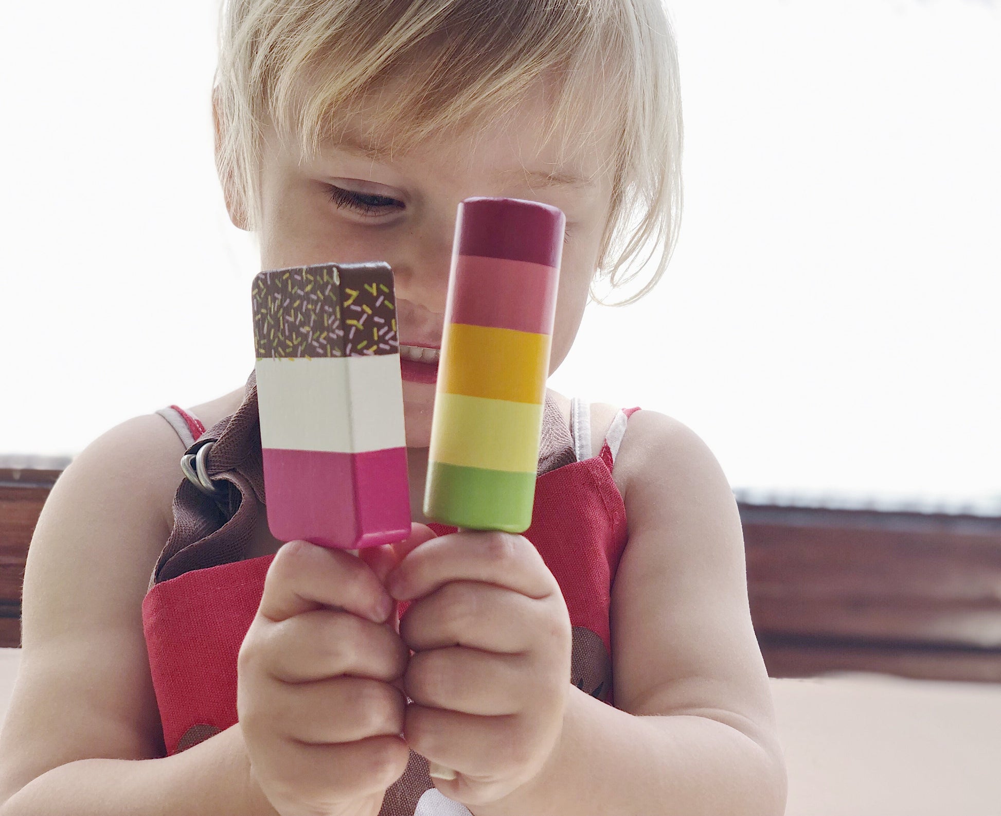 Child holding two colorful popsicles in front of their face