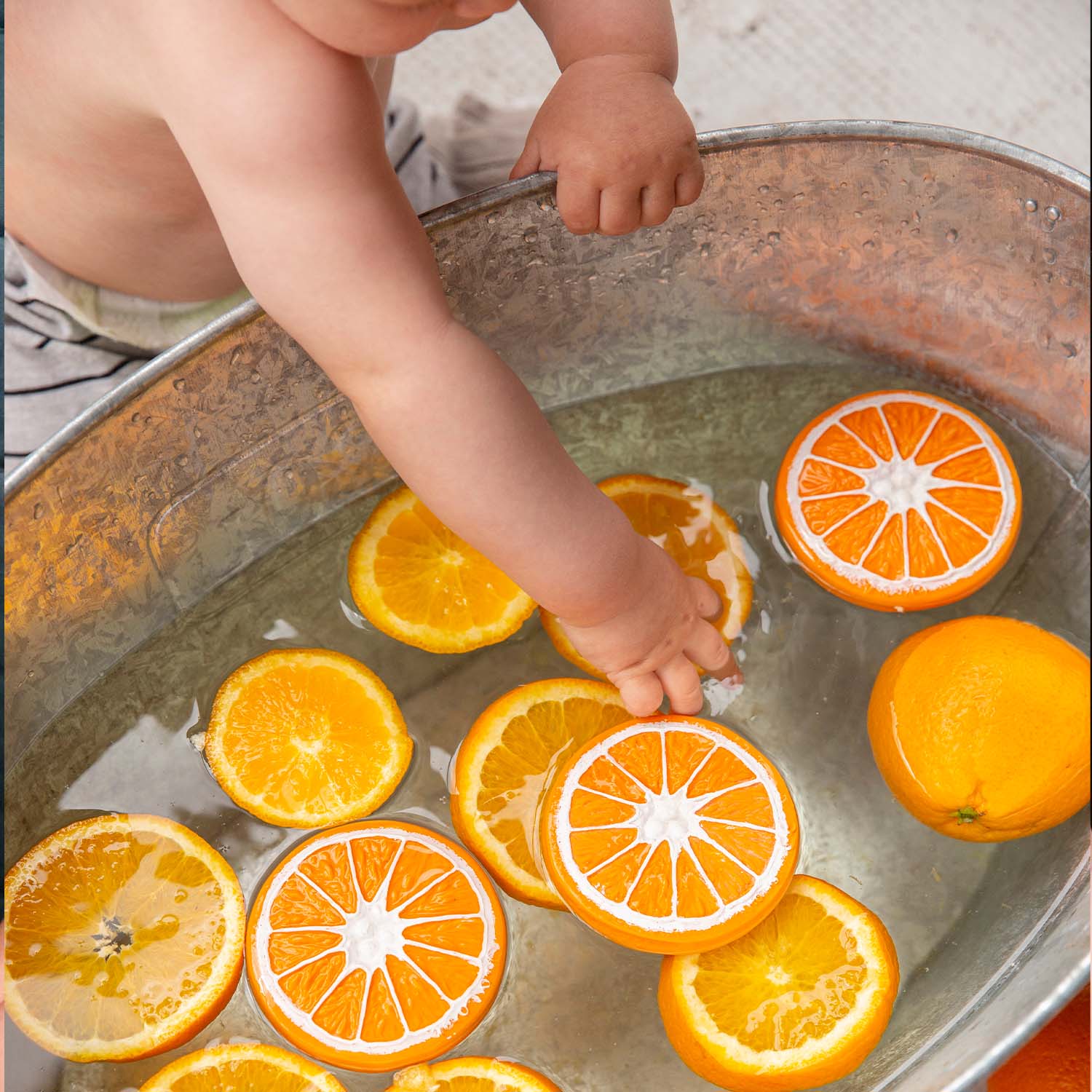 Child's hand reaching into a basin with sliced oranges.
